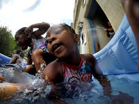 Kids frolic under the spray of a hose in a pool on the sidewalk in Trenton